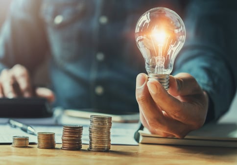 Business man holding light bulb on the desk in office and calculating on calculator