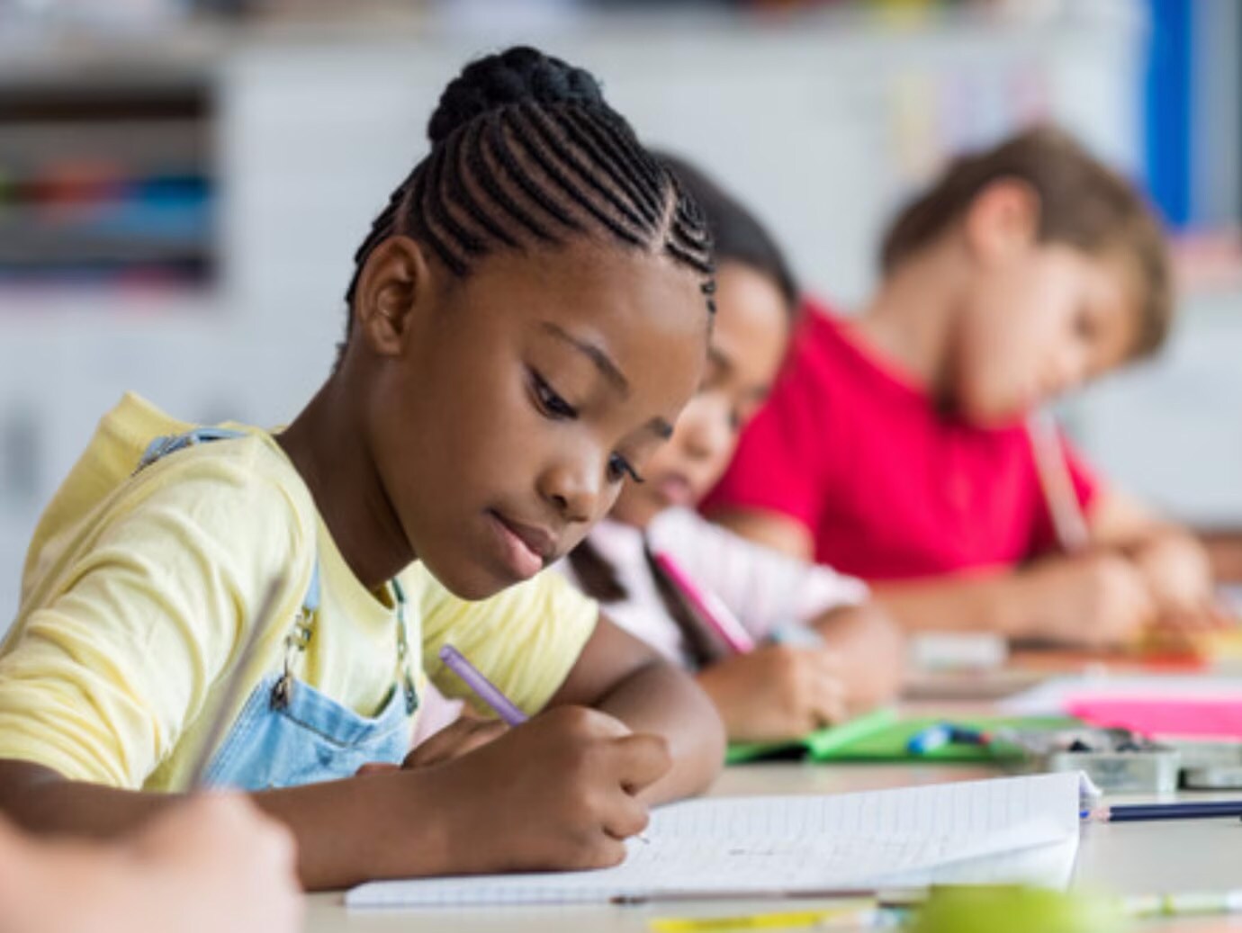 African girl writing in class with blurred background other kids writing 