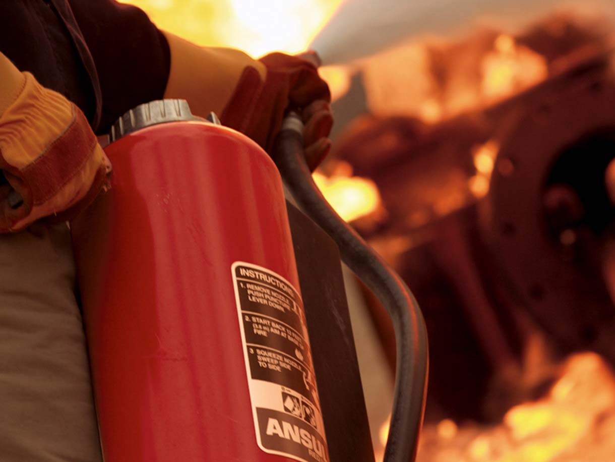 Close-up of a firefighter holding a fire extinguisher to extinguish a fire in the background