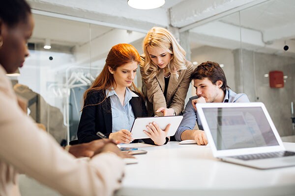 Three employees in discussion at a table, with one holding a tablet